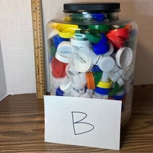 Large jar of multicoloured plastic recycled bottle caps, approximately 2 gallons